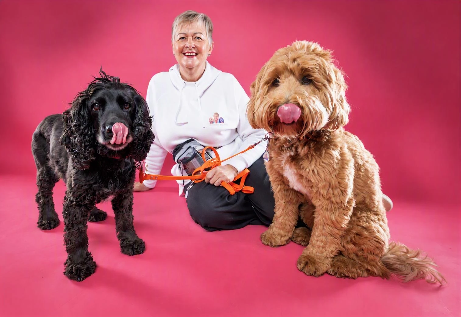 Trina sitting with two dogs against a pink studio backdrop